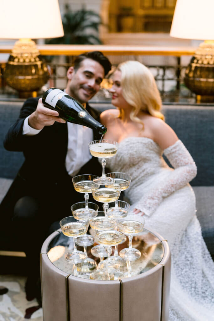 groom pouring champagne in coupes tower while bride is smiling 