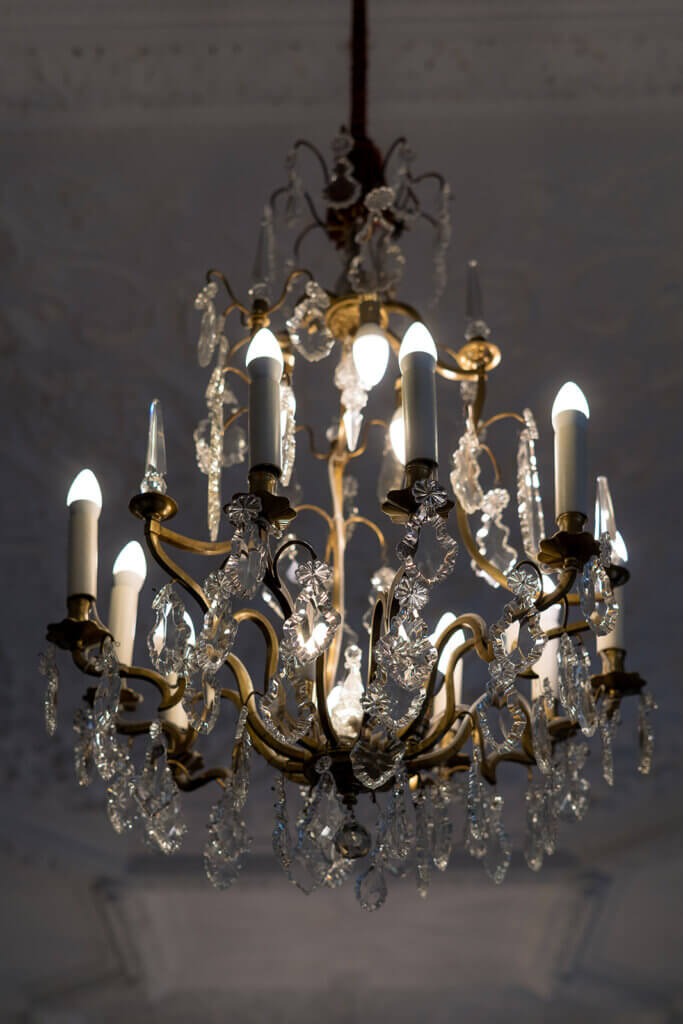 Elegant crystal chandelier with glowing candles hanging from a high ceiling, casting warm light in a refined interior.