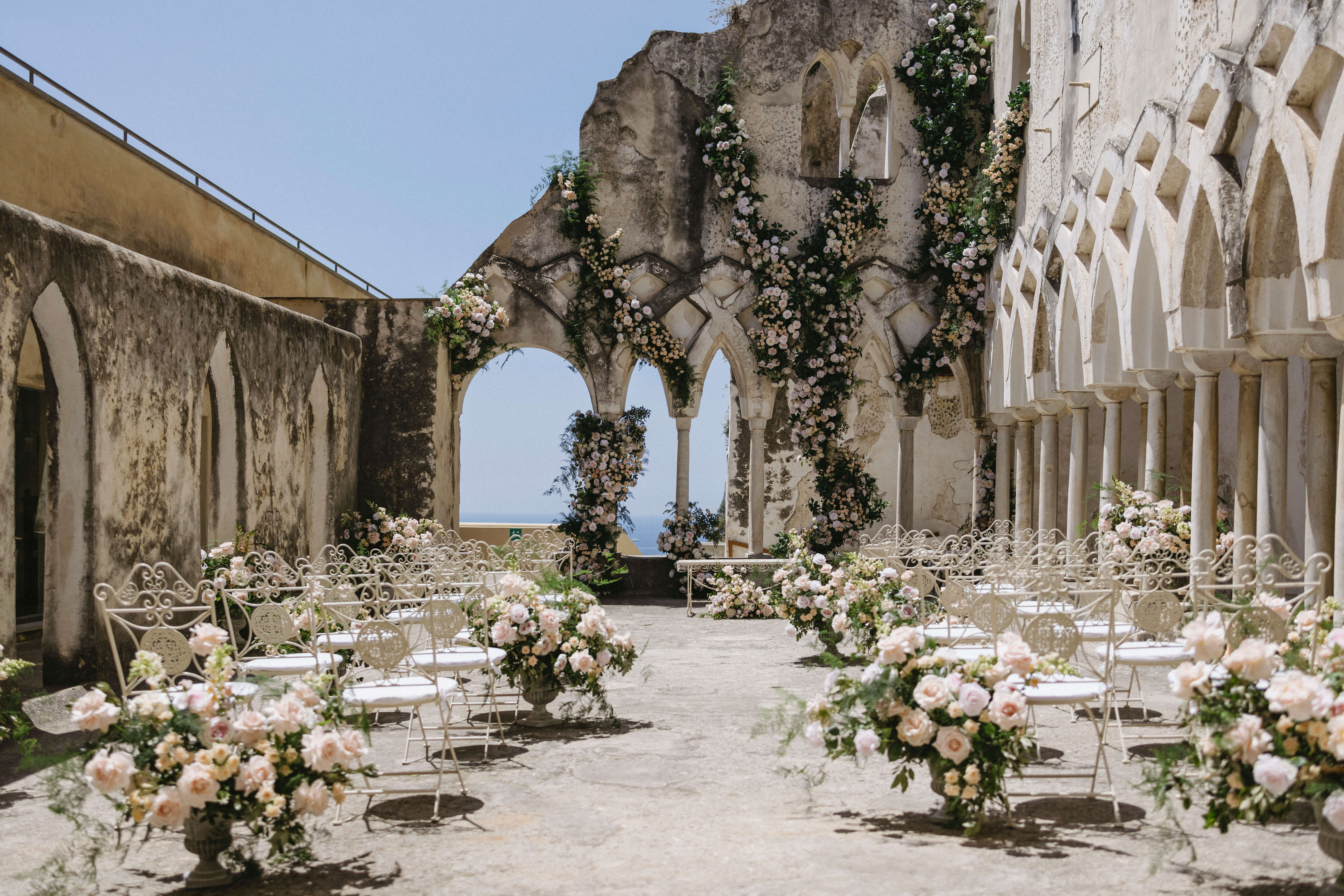 Anantara convento di Amalfi wedding ceremony with pink flowers and white metal chairs in the cloisters perfect wedding venuewith sea view