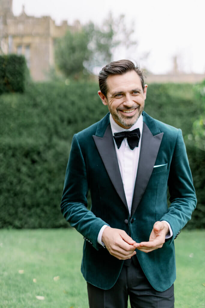 Smiling groom in a velvet green tuxedo walking in castle grounds