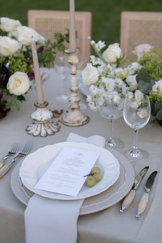 Organic luxury wedding tablescape with linen, grapes, sculptural candlelight, and artisanal glassware.