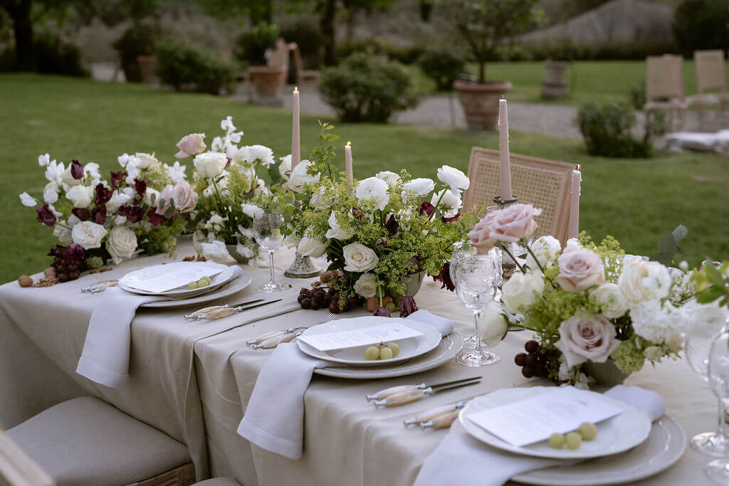 Muted autumn tablescape with taper candles and white florals arranged against a garden backdrop.